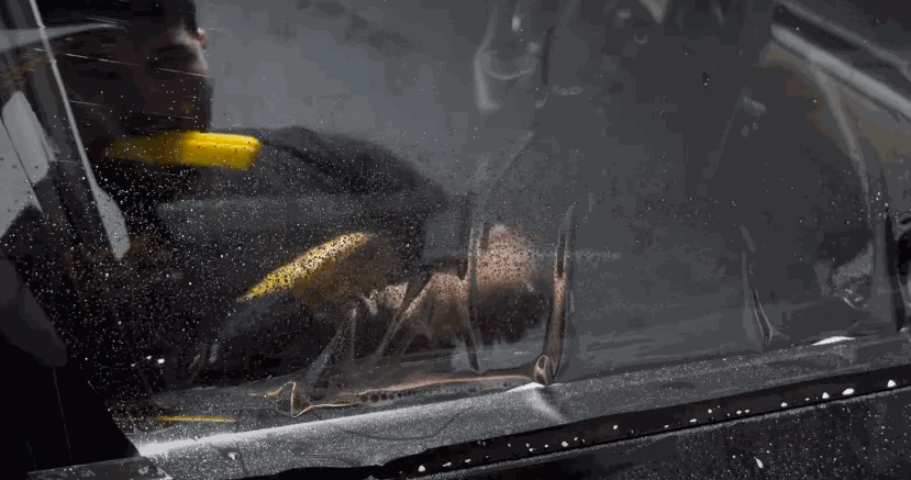 Installer uses a yellow squeegee to smooth out water and air bubbles under a freshly applied window tint film on a vehicle door.