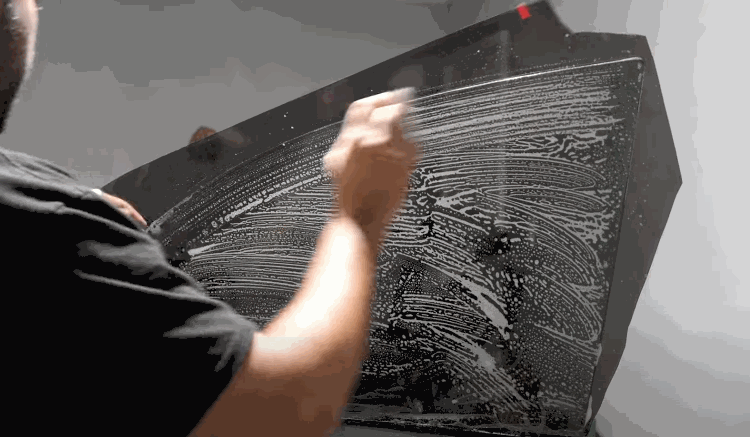 A person applies cleaning solution in sweeping motions across a car window before installing window tint film.